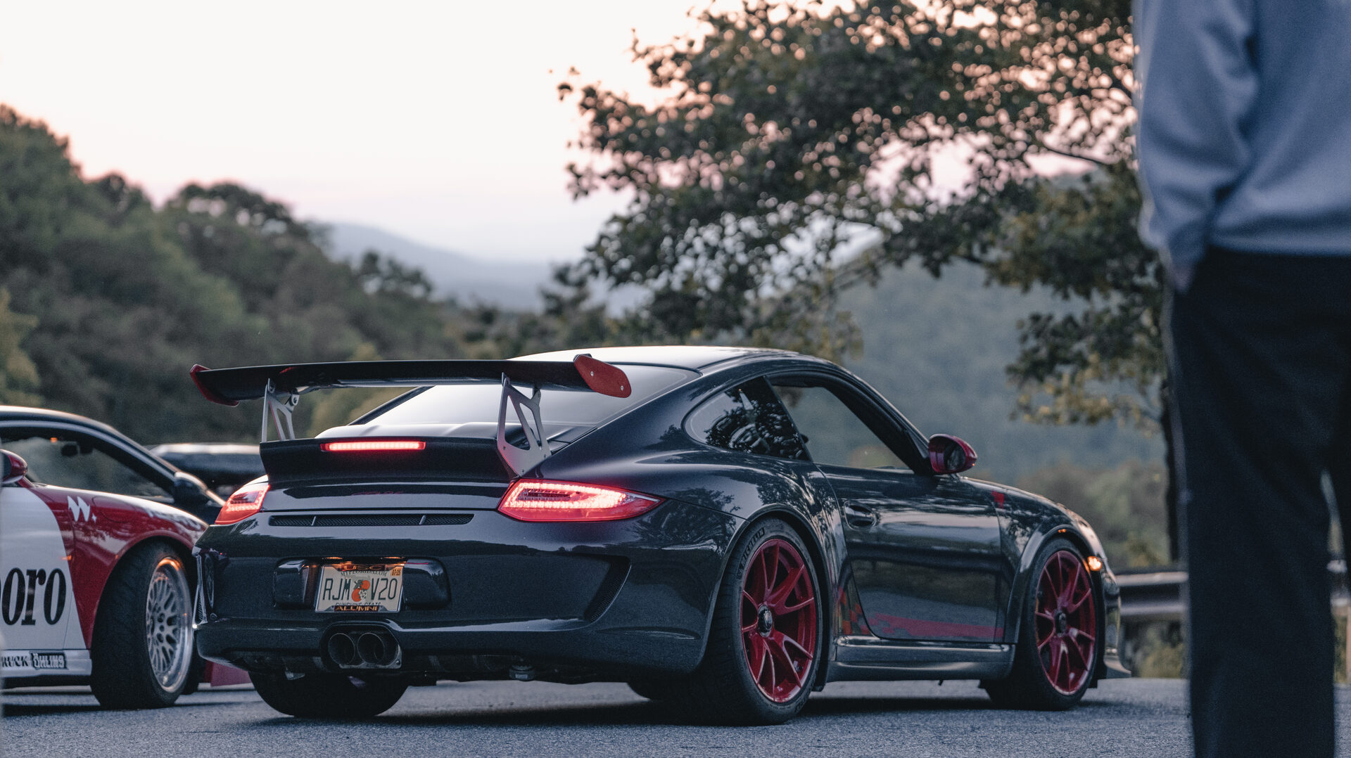 Black Porsche 911 with red wheels, rear three-quarter view