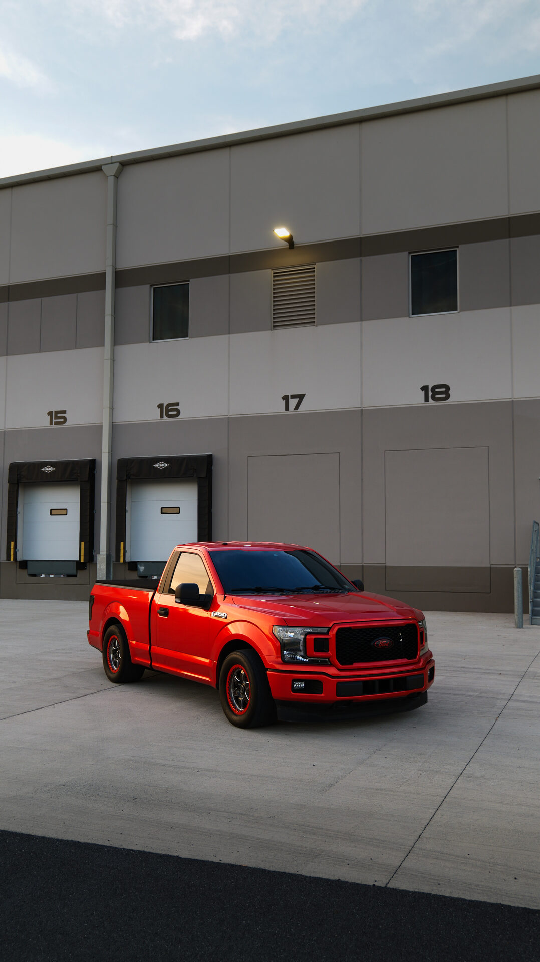 Red Ford F-150 parked in front of a loading dock at dusk