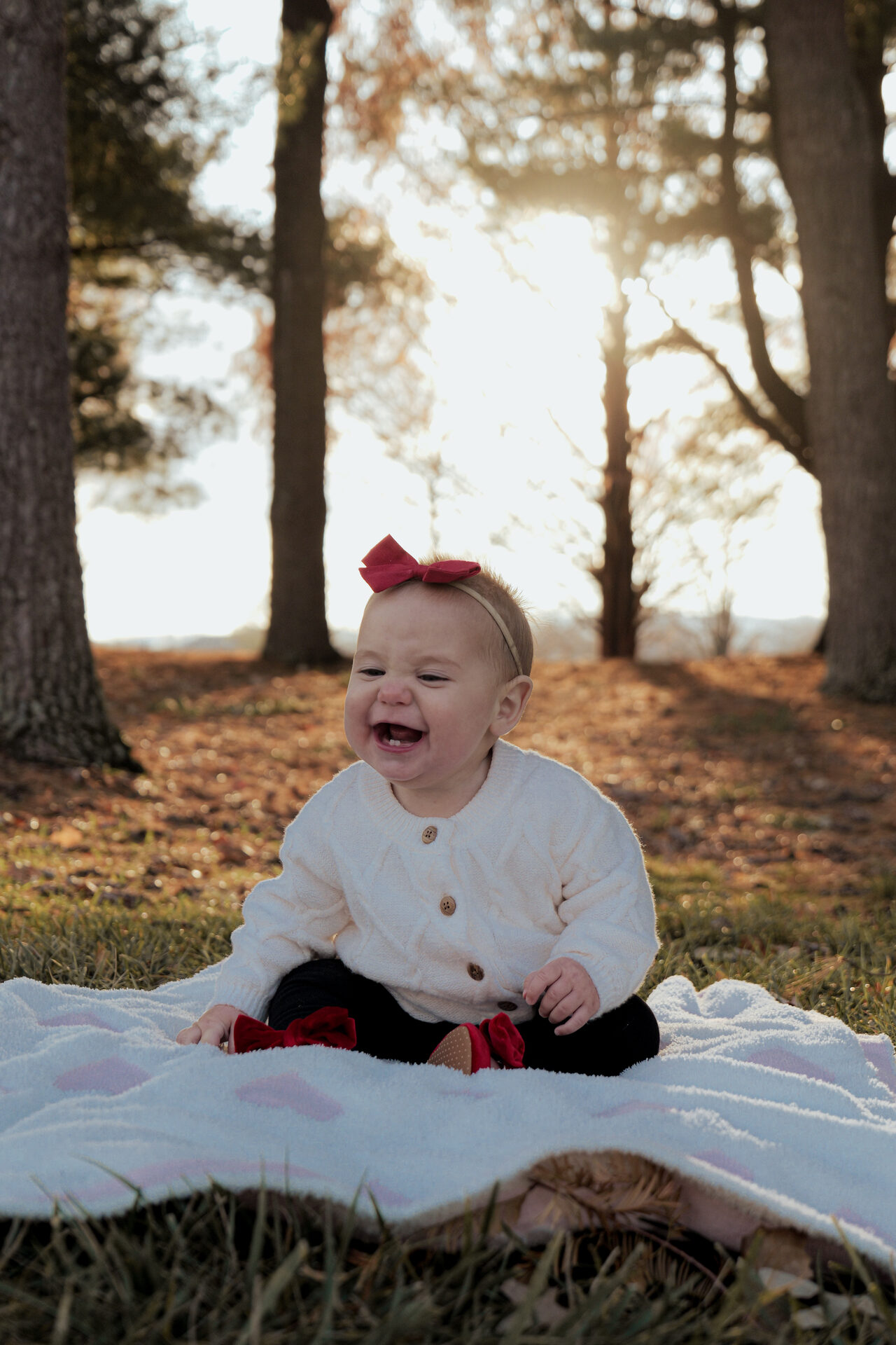 Toddler in a red bow laughing in a sunlit forest